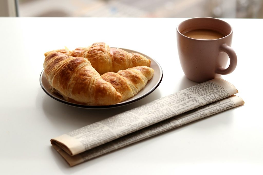 A cup of coffee served beside a fresh croissant